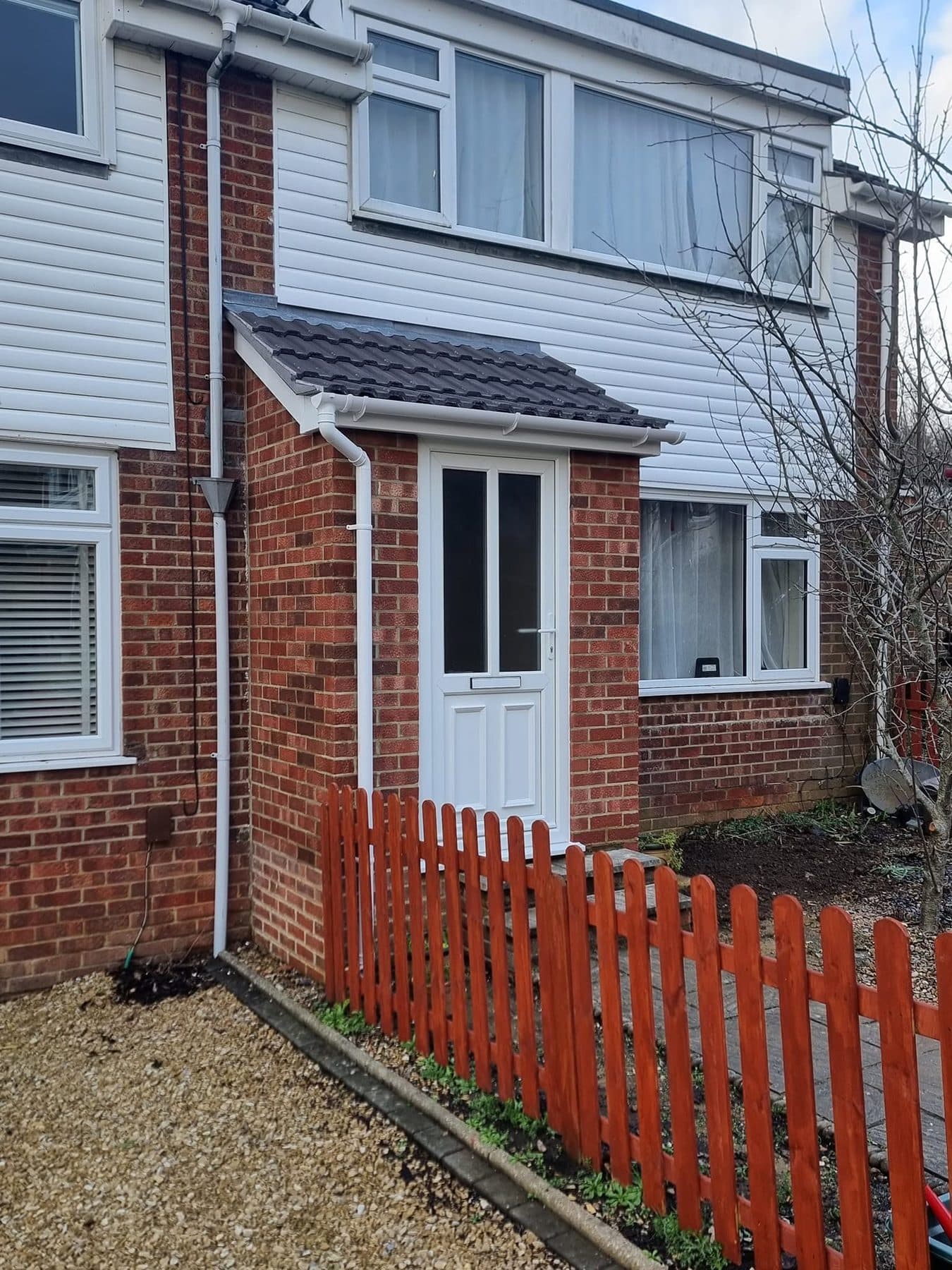 New brick front porch with a tiled lean-to roof, white uPVC door and guttering behind a picket fence
