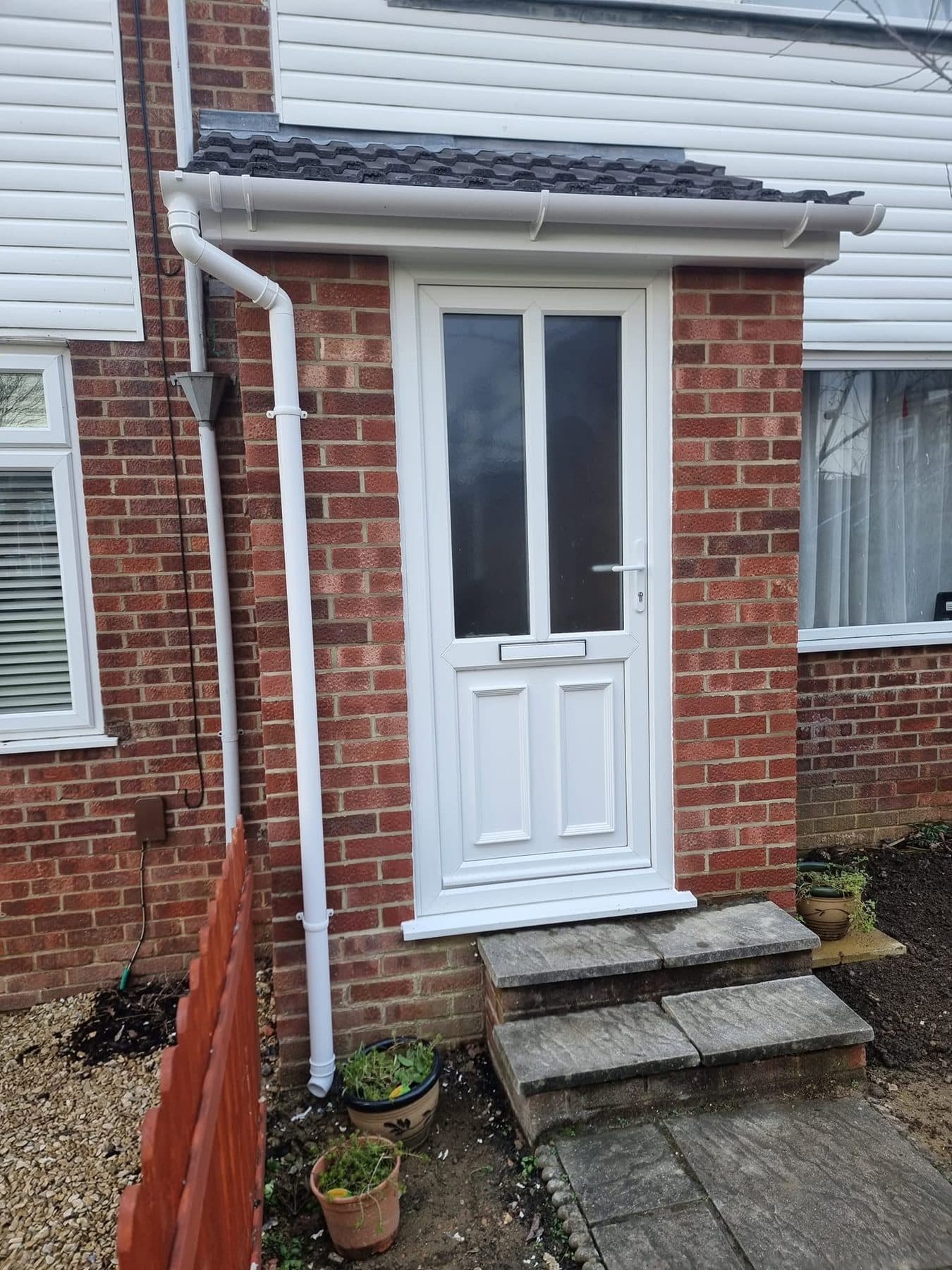 Brick porch with tiled lean-to roof, white uPVC front door, new downpipe and two stone steps