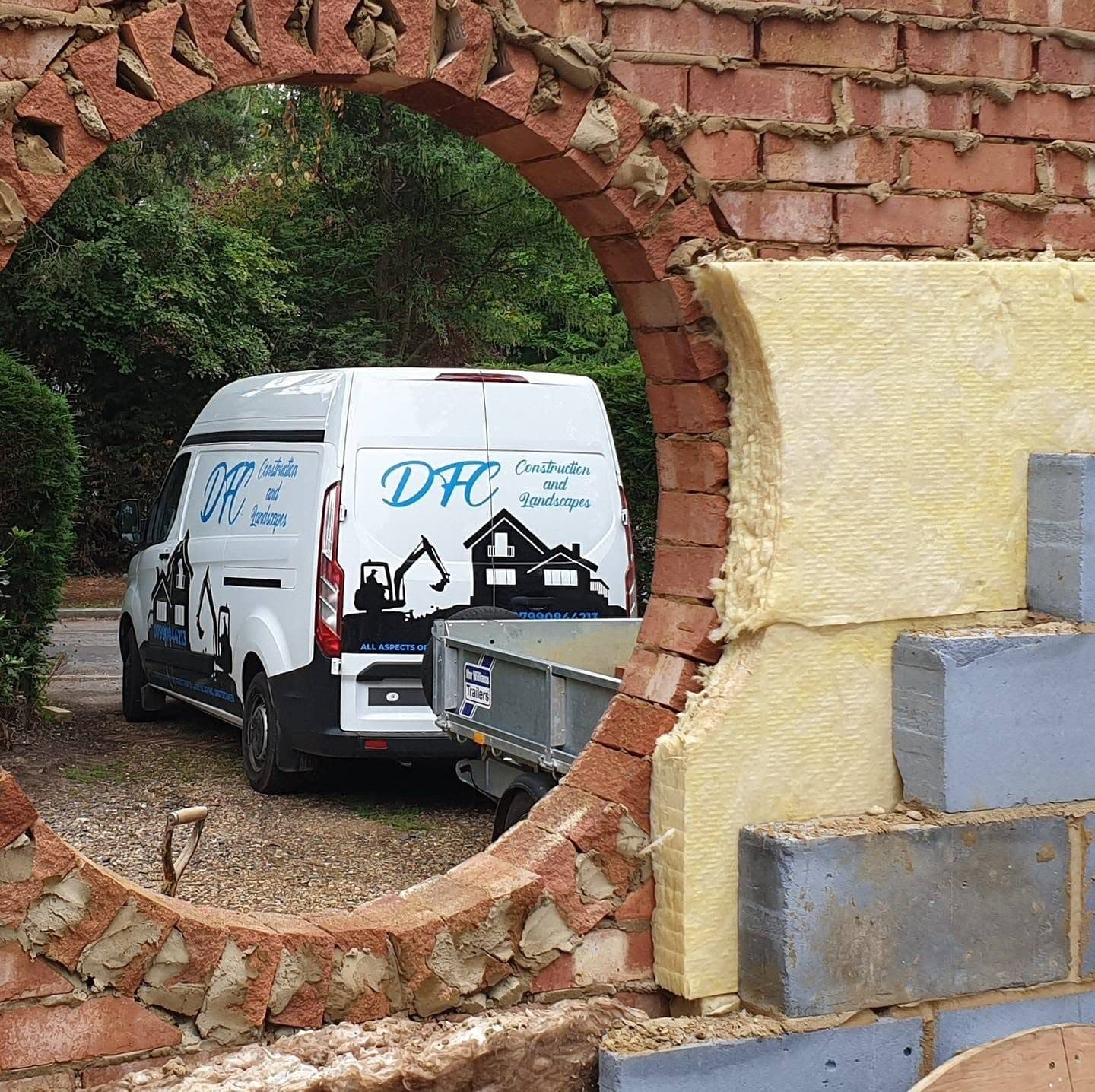 Cavity wall going up with a round brick-arched opening, insulation and blockwork inside, DFC van parked beyond