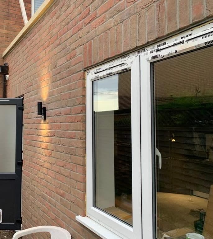 Side of a new brick extension with white uPVC French doors and wall lights