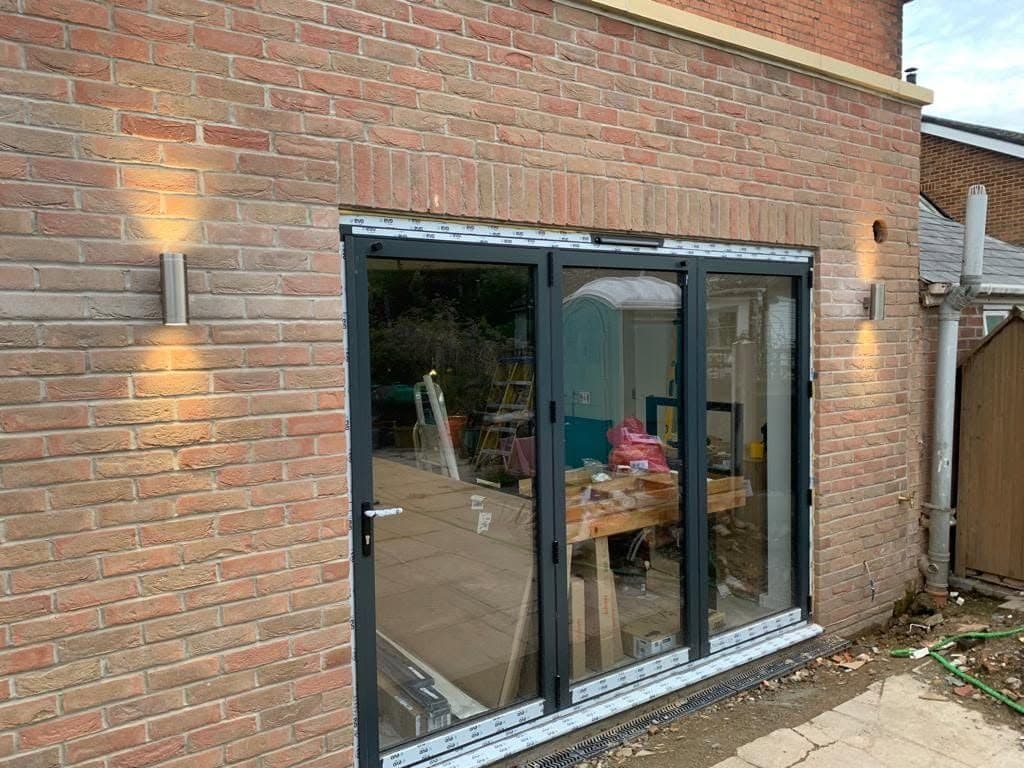 Grey bi-fold doors fitted in a new brick rear extension, with wall lights either side
