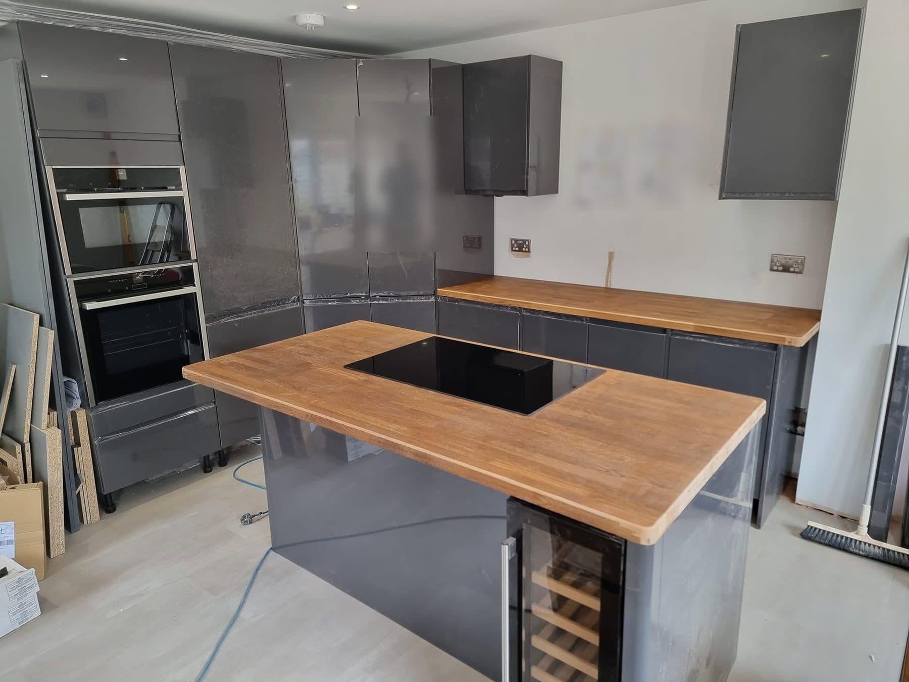 Kitchen island with oak worktop and induction hob, grey gloss units behind