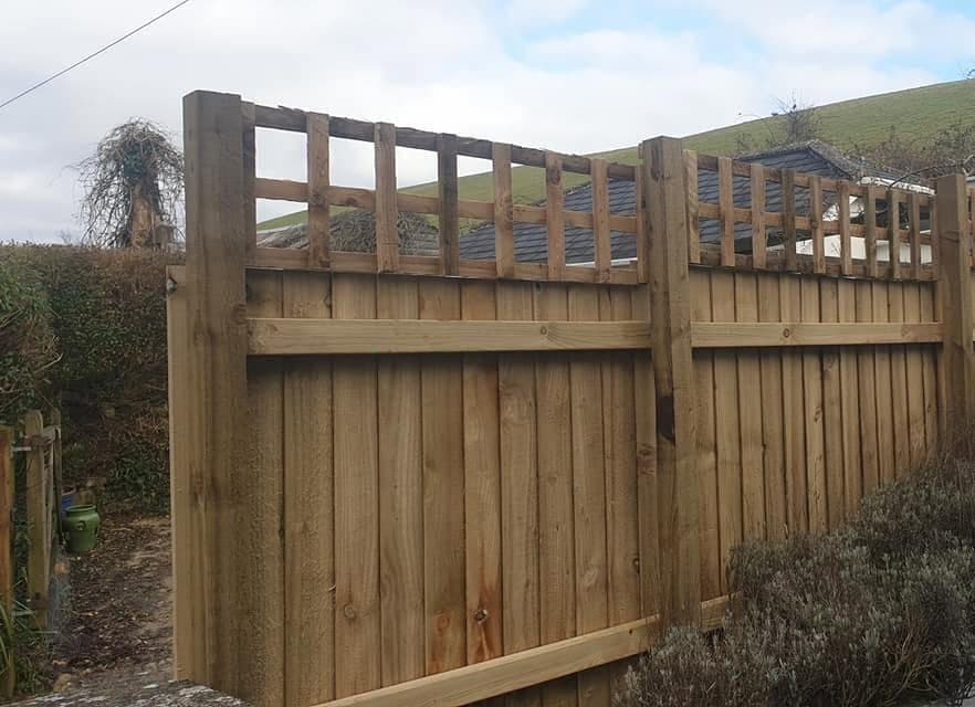 Close-board timber fence with a square trellis topper behind a lavender bed, hillside beyond