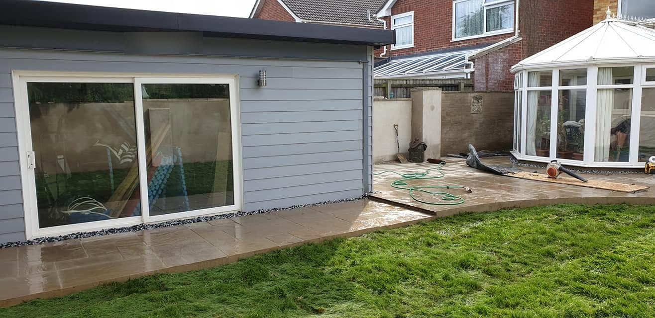 Grey-clad garden room with sliding doors, sandstone patio wrapping round it and new turf in front