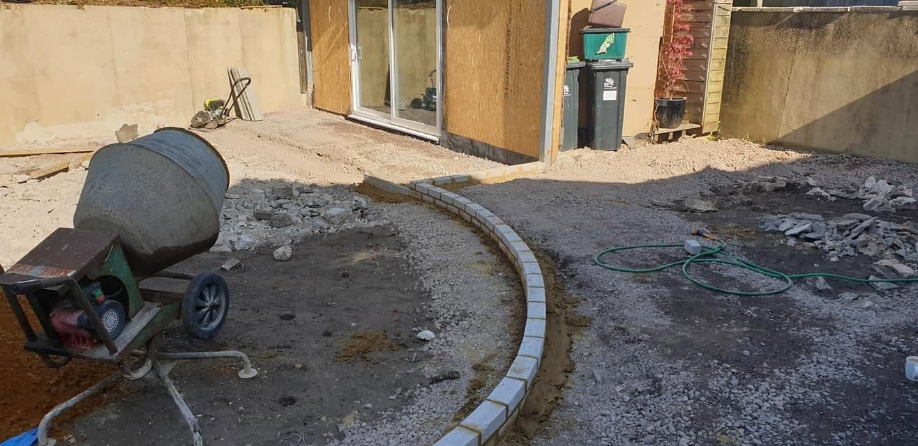 Curved block edging set in concrete on a stone sub-base, garden room shell behind, mixer in the foreground