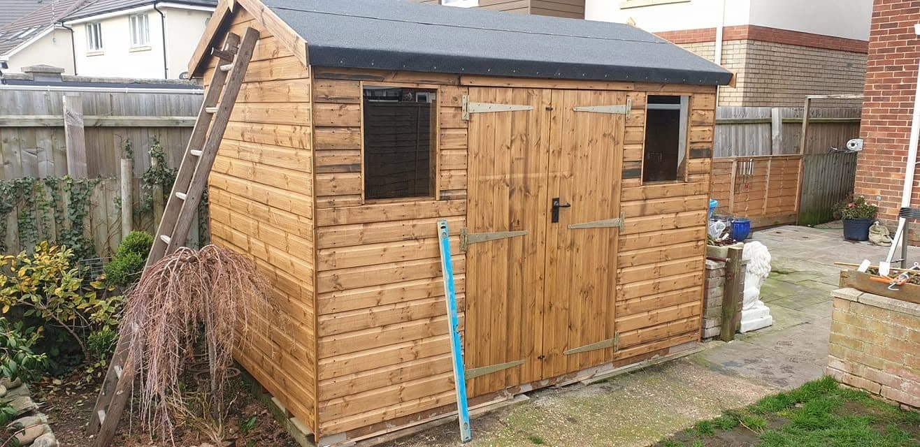 Apex timber shed with double doors and felt roof, built on an existing base in a back garden