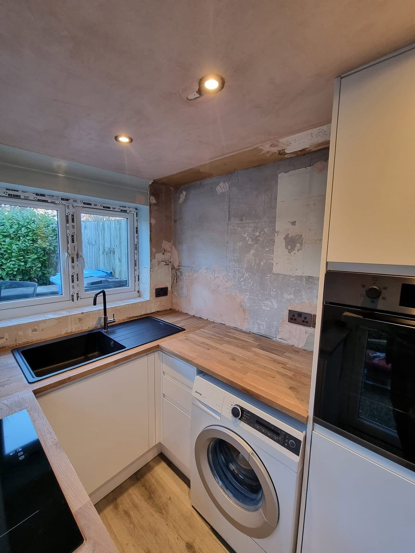 New kitchen with white handleless units, oak worktops, black sink and a built-in oven