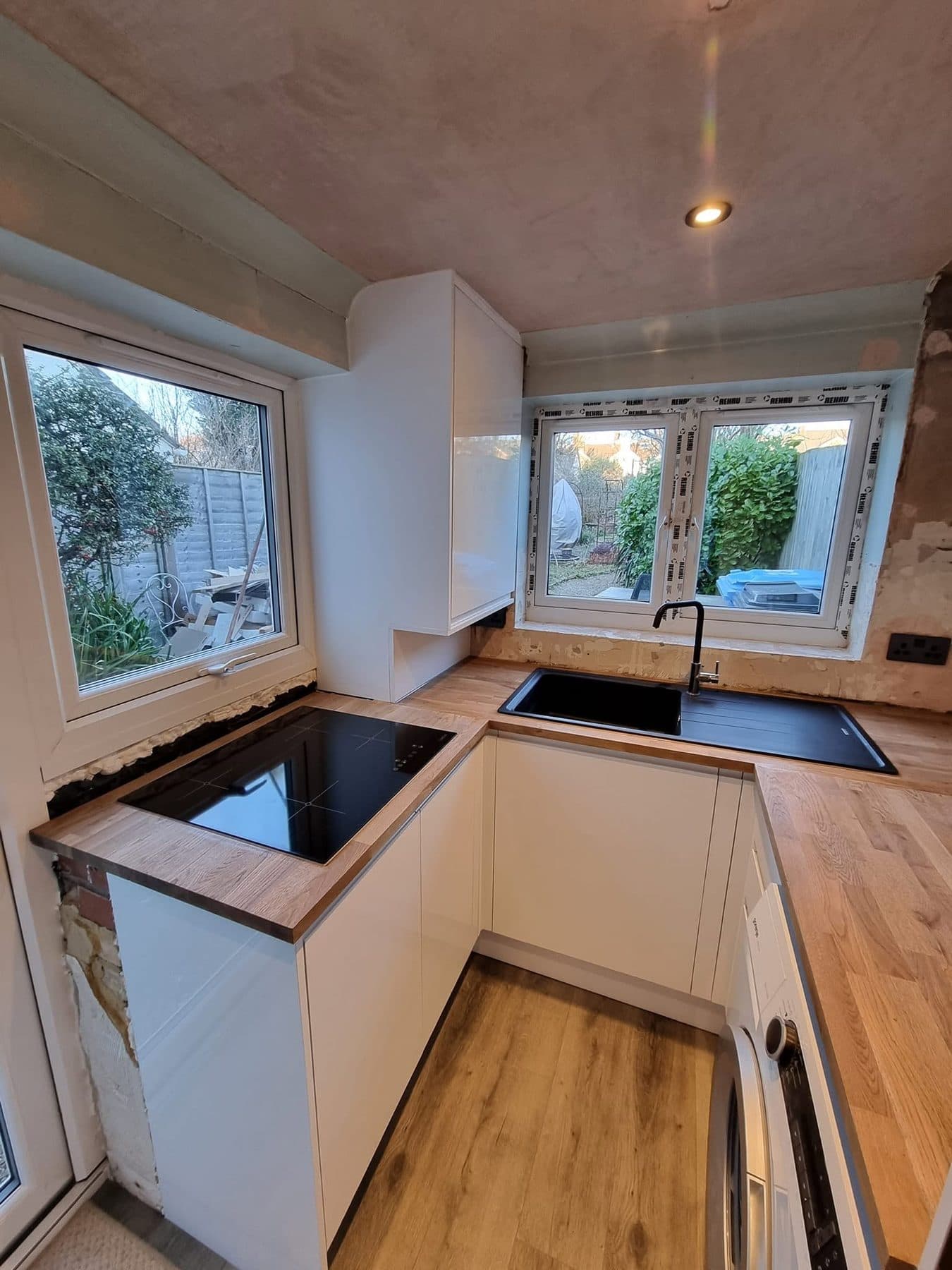 Corner of a new kitchen with oak worktops, induction hob and black sink under new windows