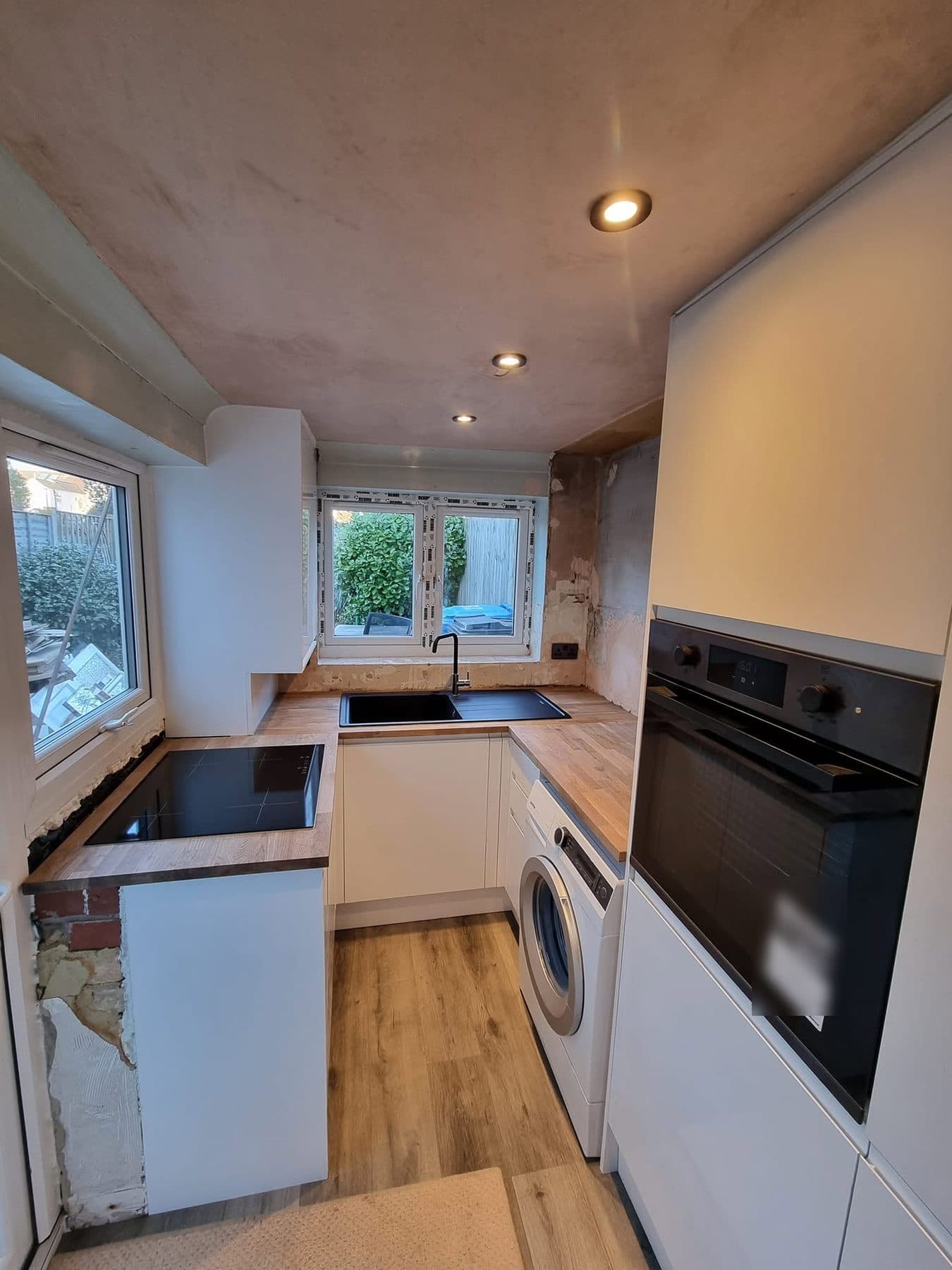 Refitted galley kitchen with white units, oak worktops, oak-effect floor and built-in oven