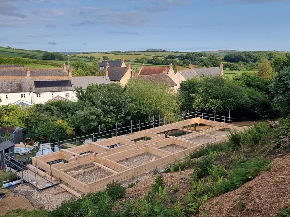 Timber base frame and first log courses for a log building on a gravel pad, seen from above