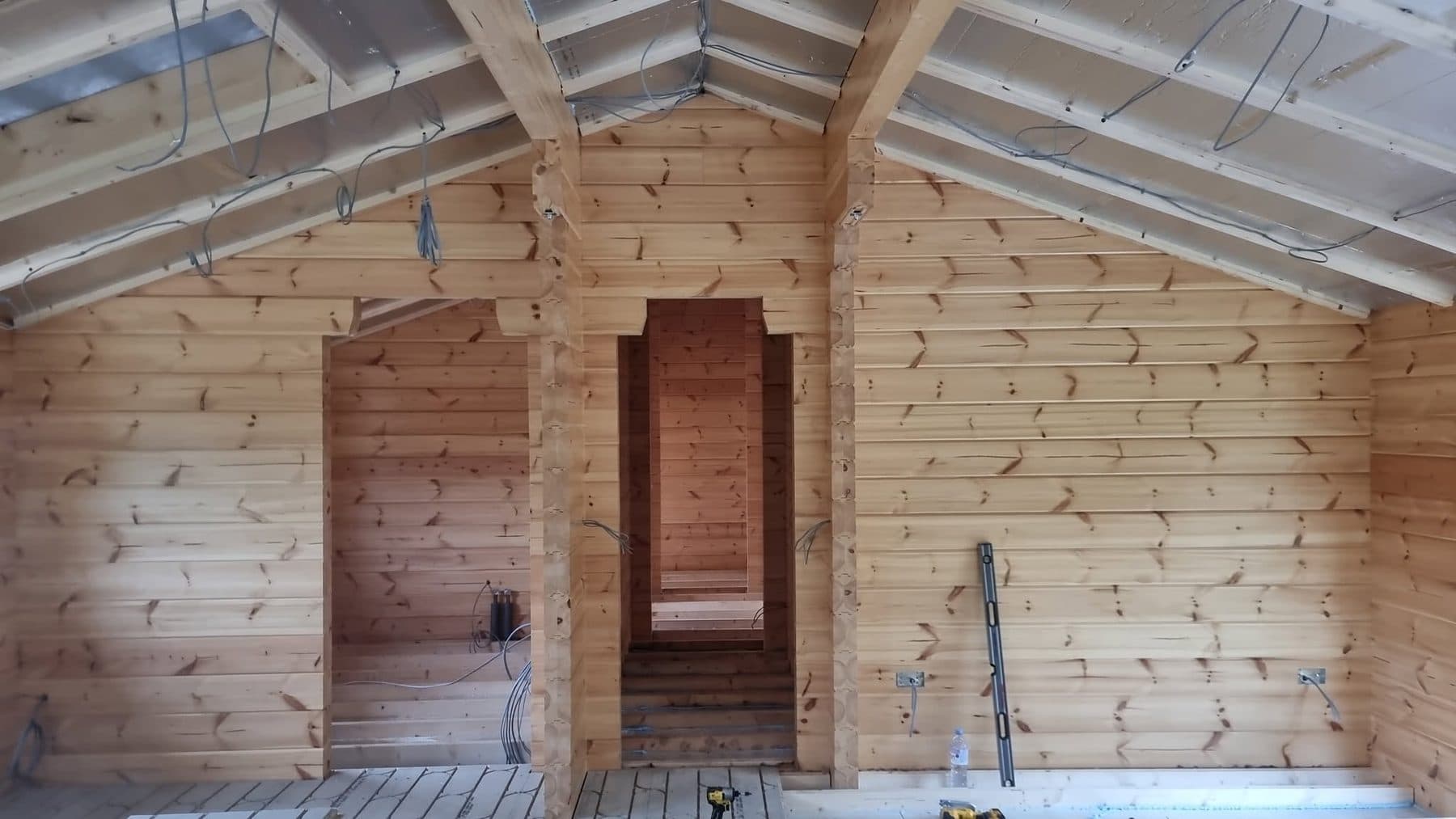 Log cabin interior mid-build: insulated vaulted roof, first-fix cables, log partitions with door openings
