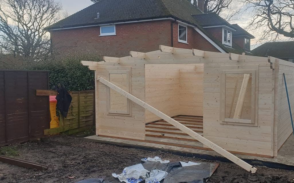 Timber log cabin under construction on a concrete base, walls up and roof purlins fitted, ready for roof boards