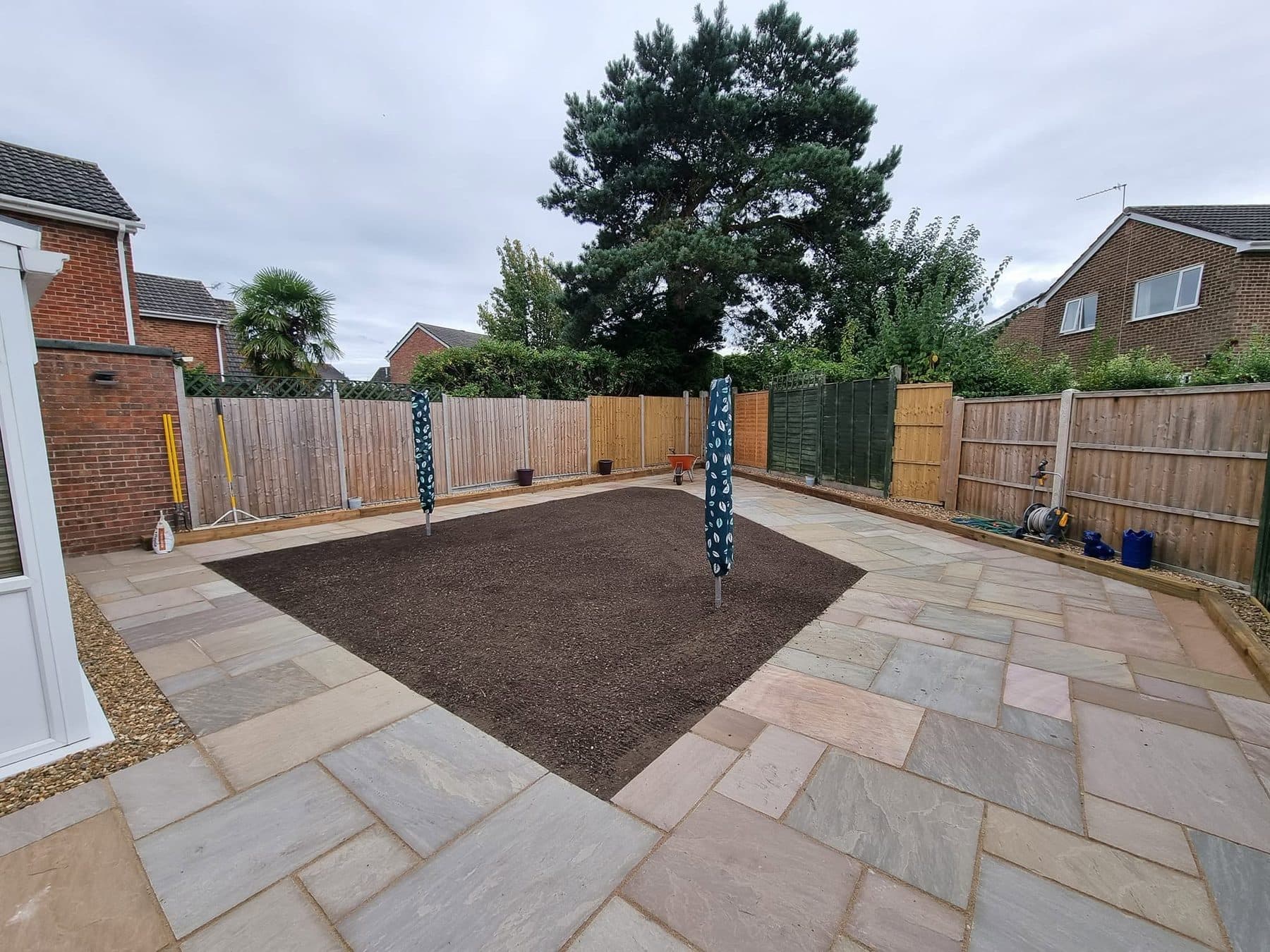 Sandstone patio laid around a prepared lawn bed, with sleeper-edged gravel borders and timber fencing
