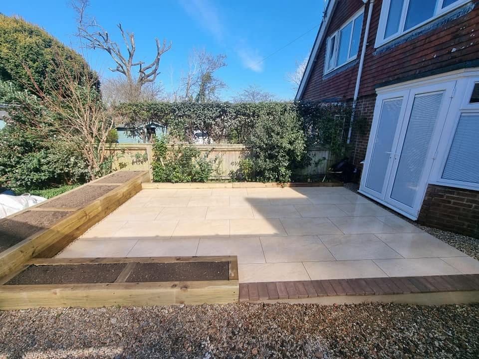 Pale paved patio outside French doors with timber sleeper raised beds and a brick edge