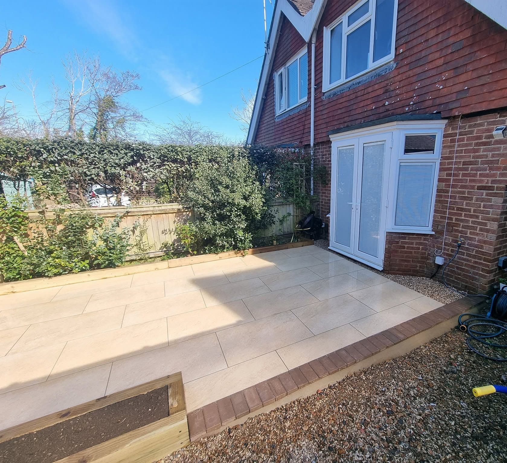 Finished pale paved patio outside French doors, brick paver edging and a timber sleeper raised bed