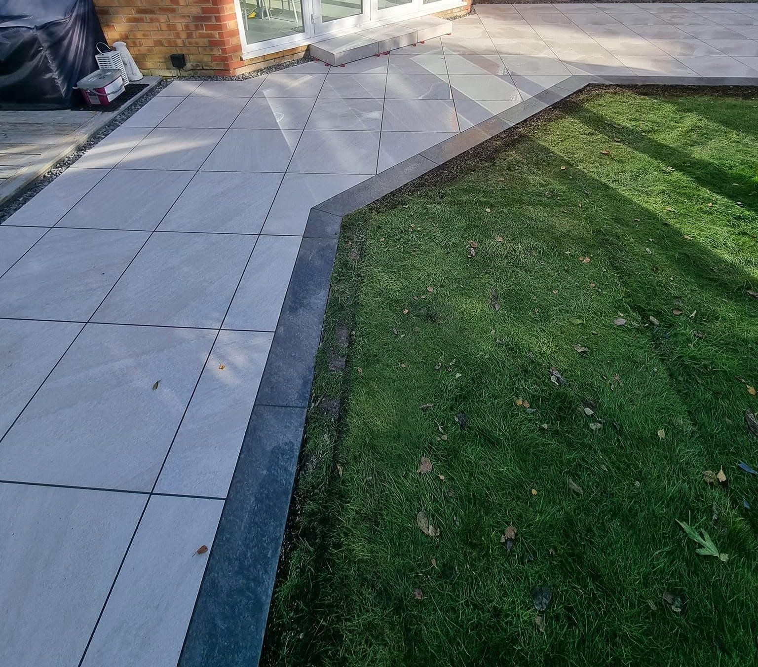 Light grey porcelain patio with a dark grey border and an angled edge to the lawn