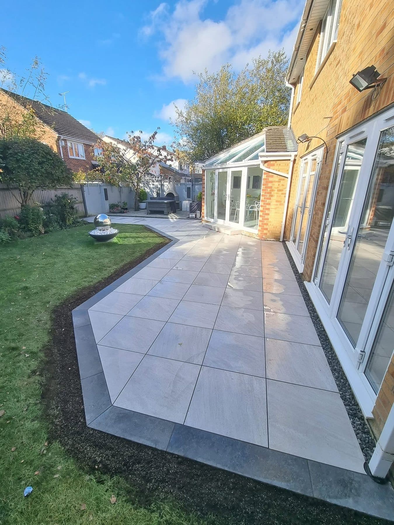 Porcelain patio with a dark grey border along the back of a house, lawn and garden beyond