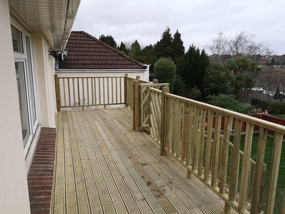 Finished raised timber deck along the back of a house, with spindle balustrade and a braced gate to the garden