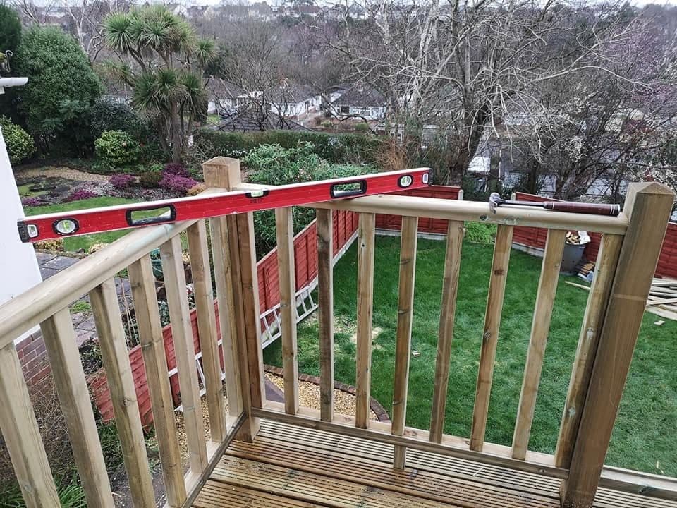 Corner of a timber deck balustrade under construction, spirit level on the rail, garden below
