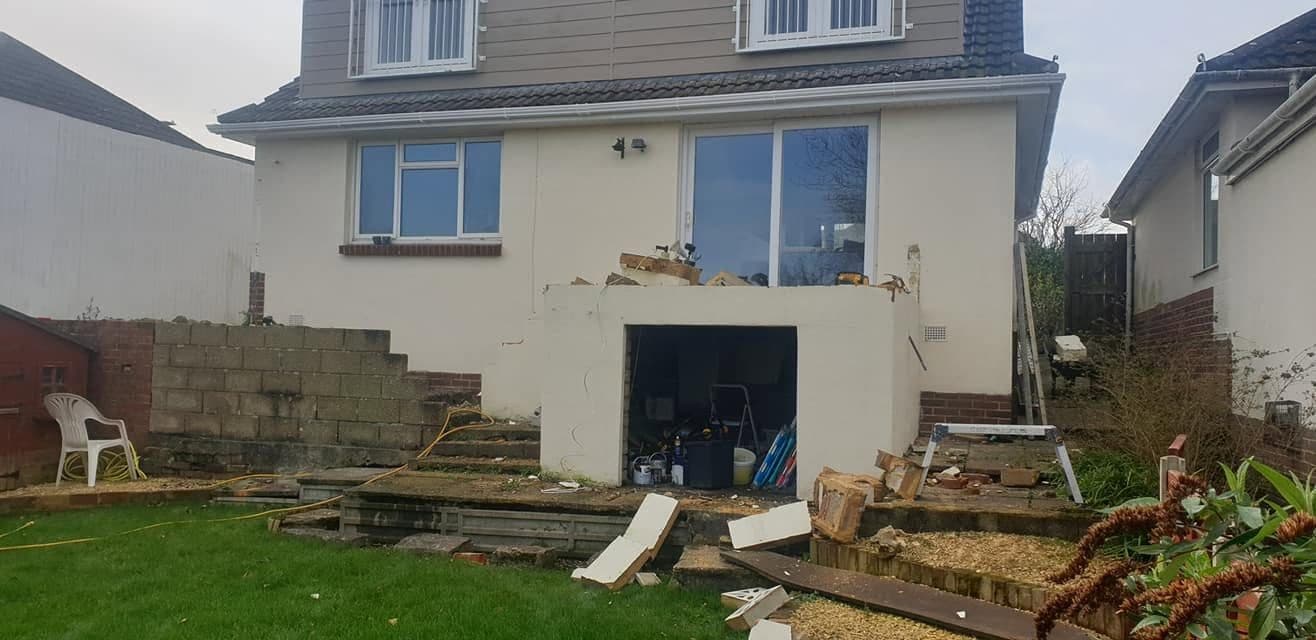 Back of a house before the deck build, with old concrete steps, a rendered store and building debris