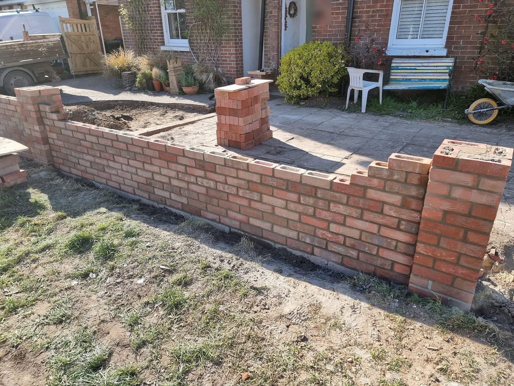 Front garden wall in red facing brick part built, with piers and stacked bricks ready on the path