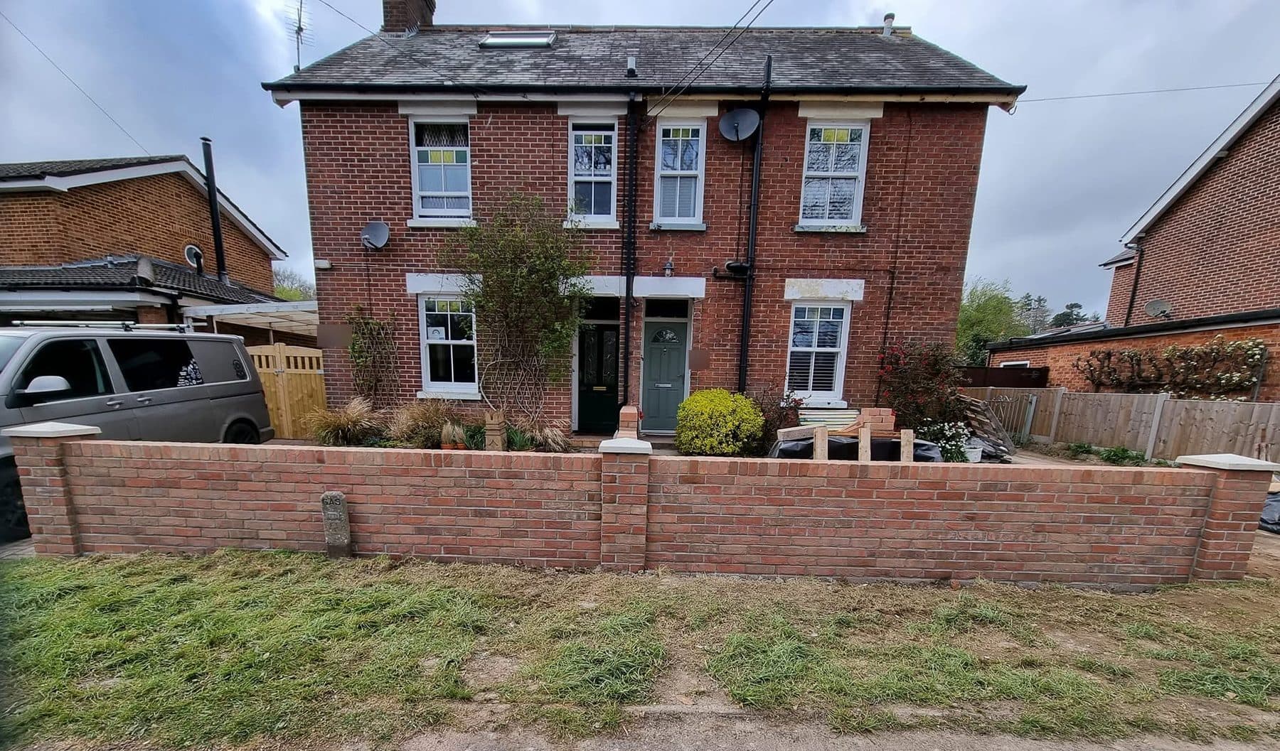 Finished red brick front garden wall with piers and coping stones in front of a pair of brick houses
