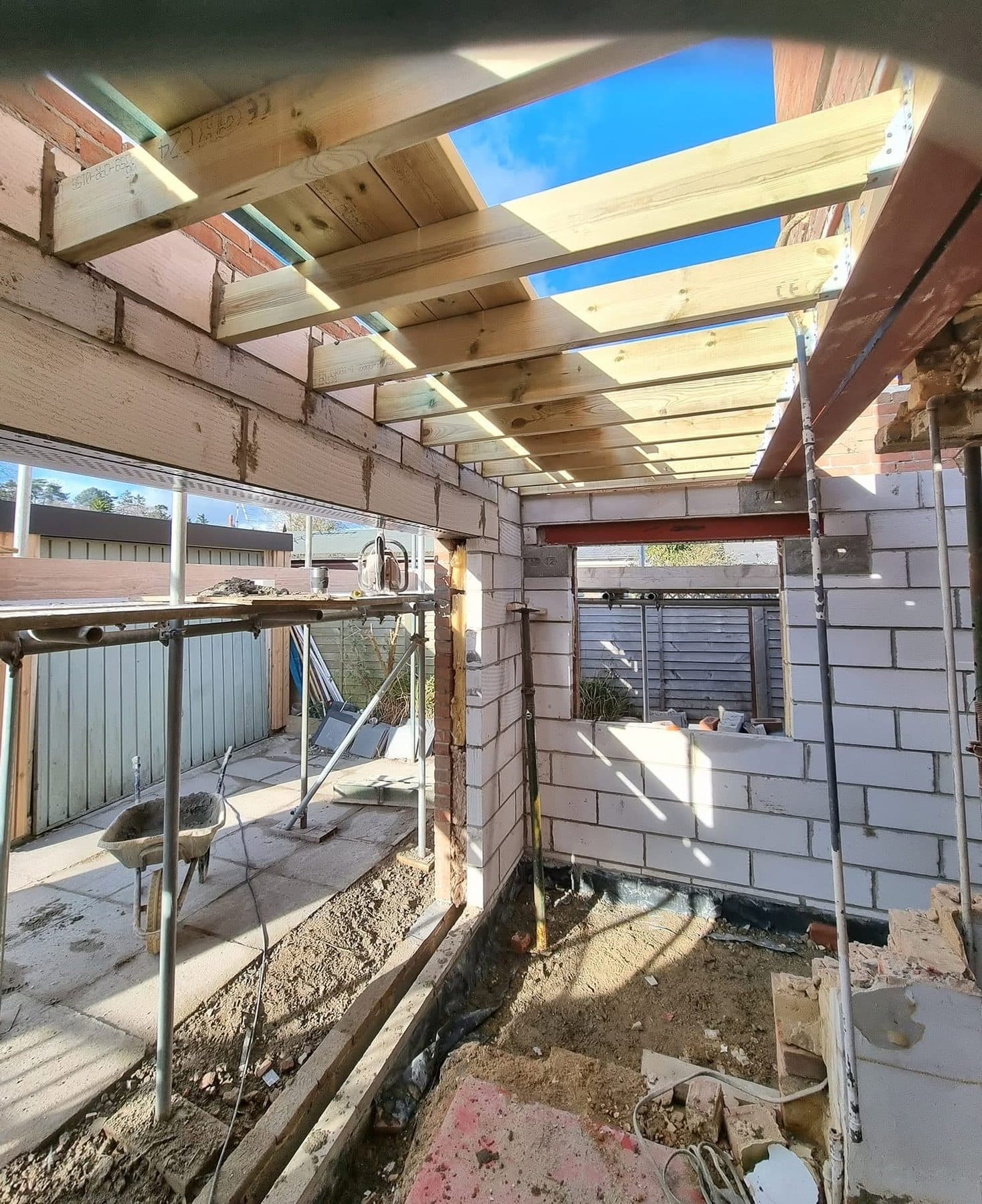 Inside a single-storey extension shell, timber roof joists over blockwork walls with a steel lintel above a window opening