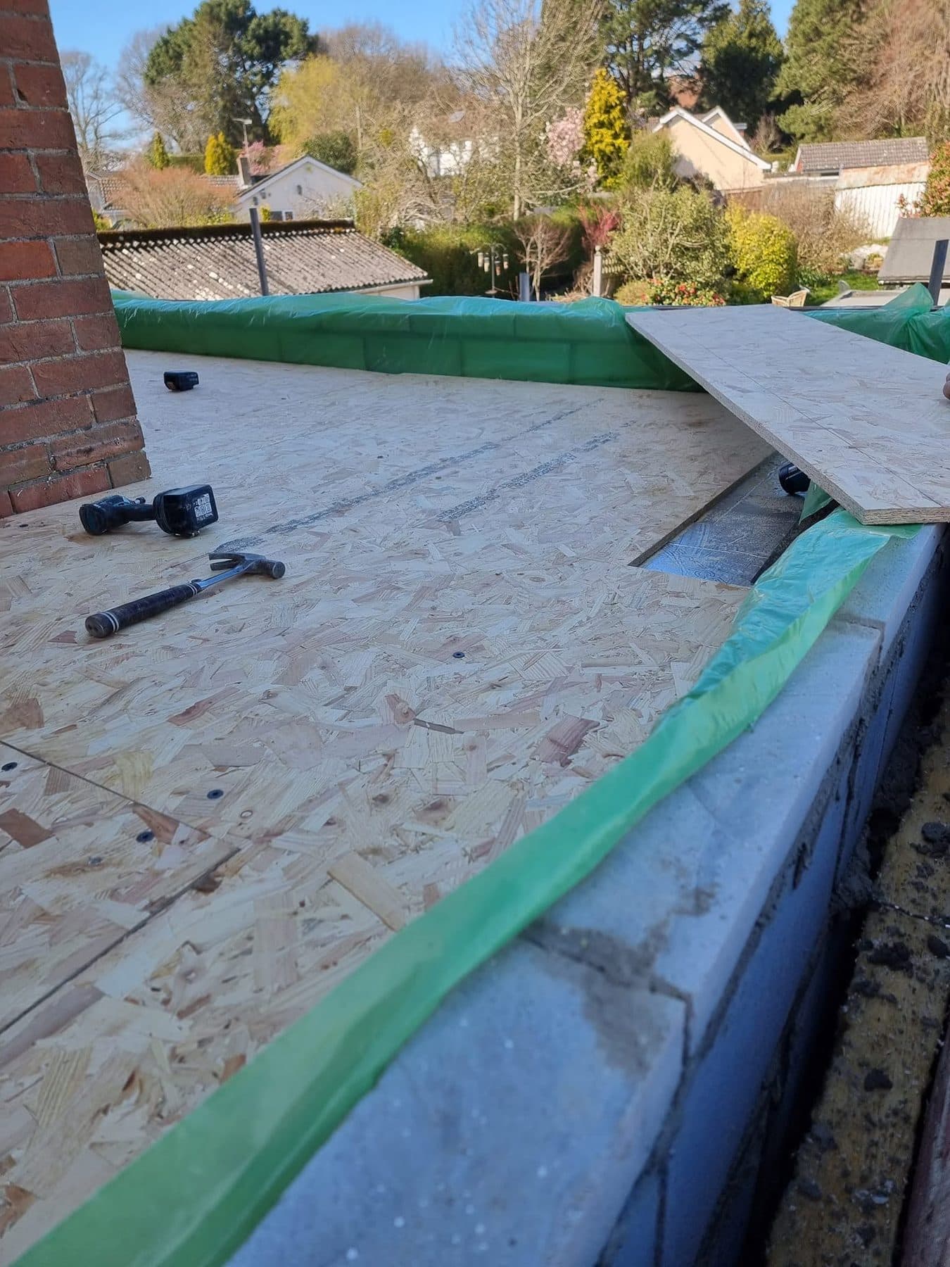 OSB boards being fixed to form a flat roof deck on a new extension, with tools on the deck