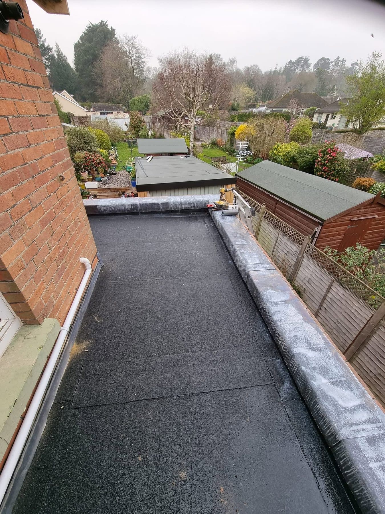 Finished black felt flat roof on a single-storey extension, edges dressed over the kerb