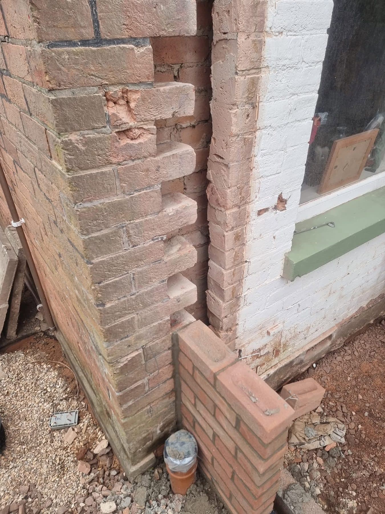 Existing brick corner toothed out to bond in new facing brickwork for an extension, with a capped drain pipe