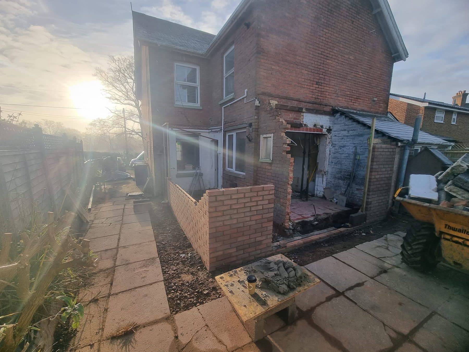 Rear of a red brick house with new extension walls part built and an opening formed in the old lean-to