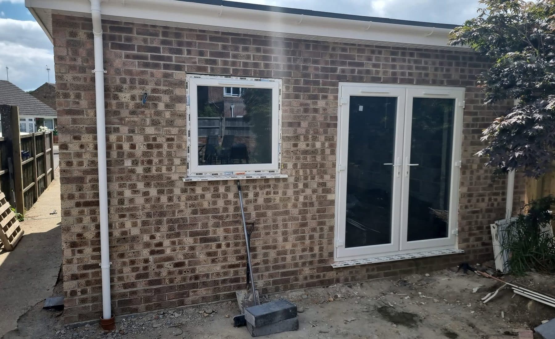 Single-storey brick rear extension with flat roof, new uPVC window and French doors, ground not yet laid