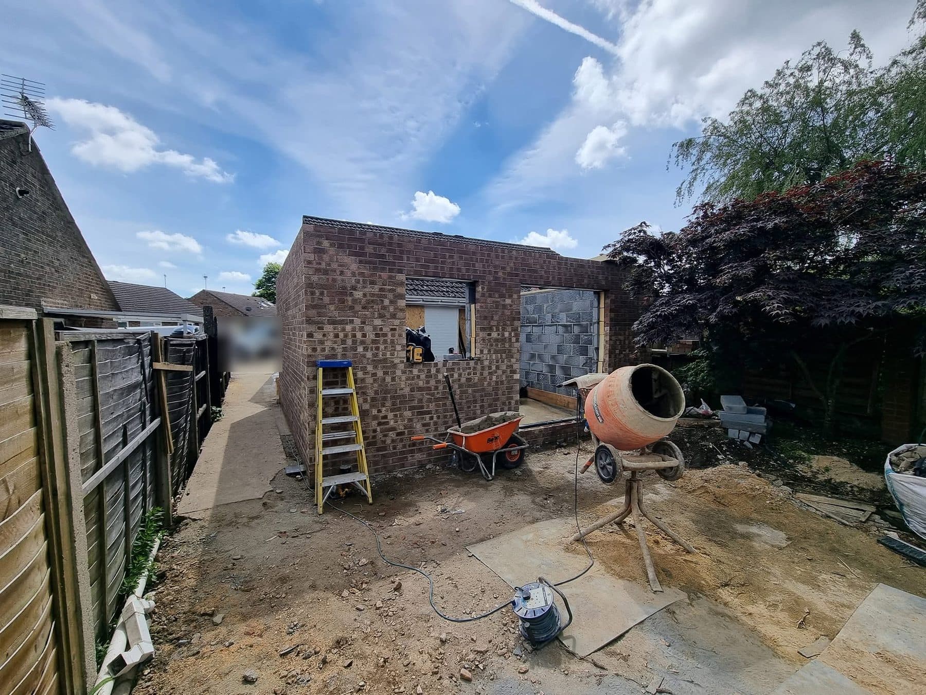 Brick shell of a single-storey rear extension built to roof height, with ladder, barrow and mixer