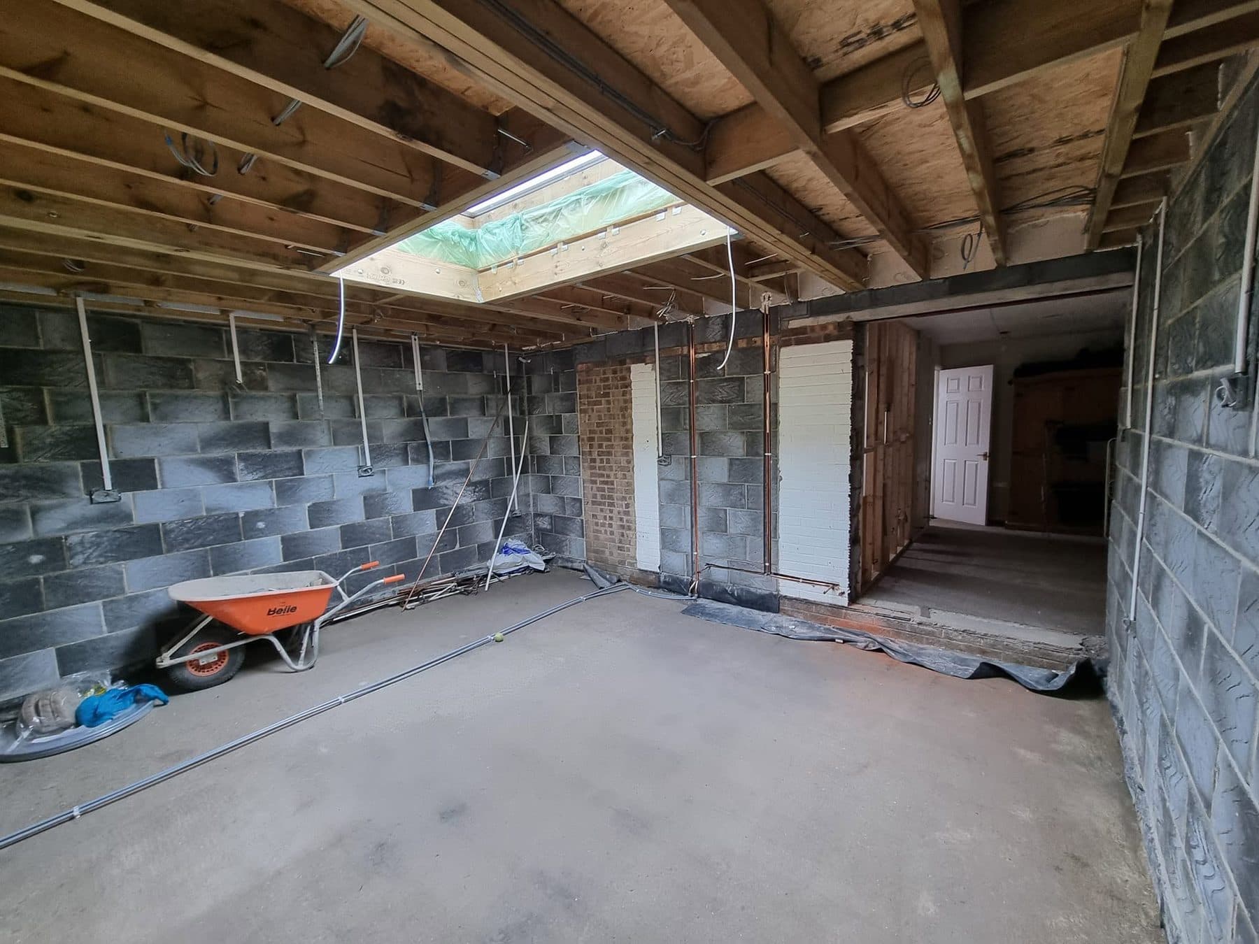 Inside an extension shell: blockwork walls, timber roof joists, rooflight opening and knock-through to the house