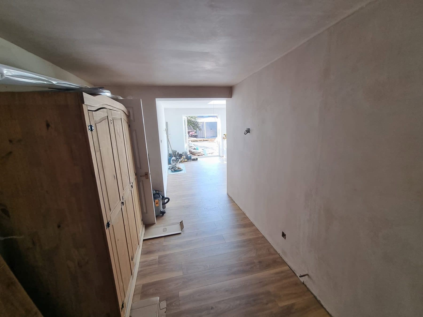 Freshly plastered hallway with new wood-effect floor leading through a new opening into the extension