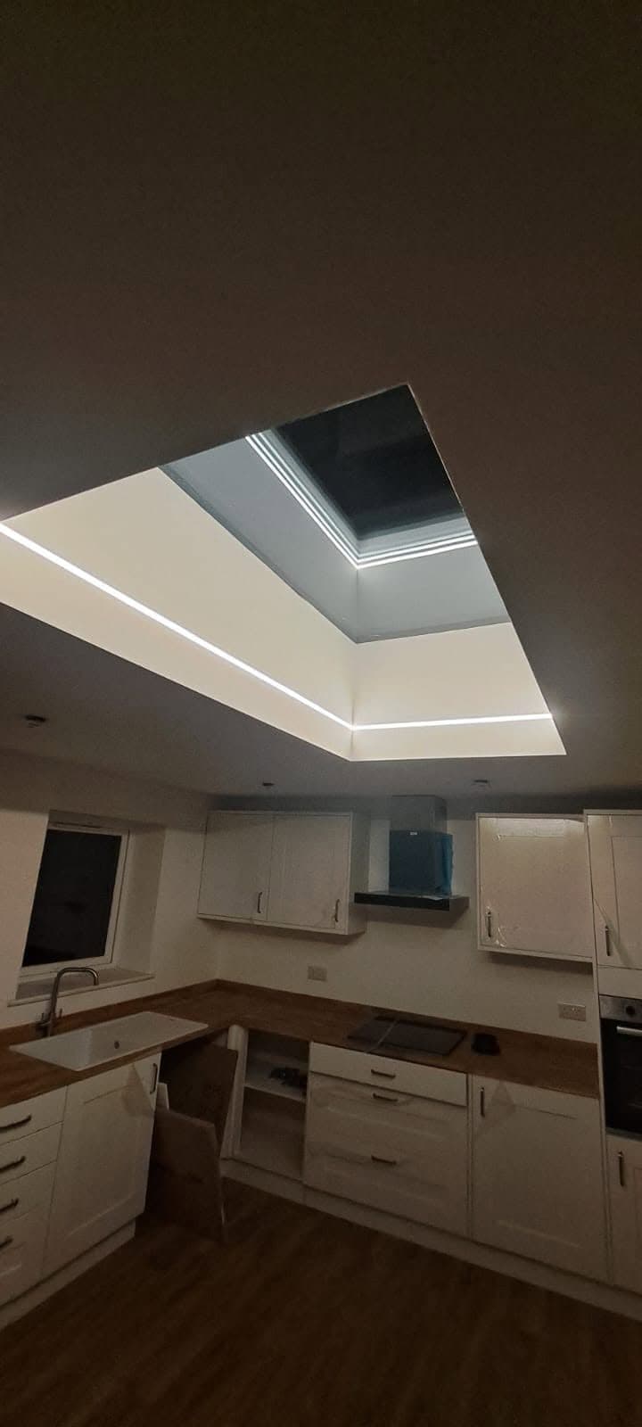 Flat rooflight over a new kitchen with LED strip lighting around the opening, at night