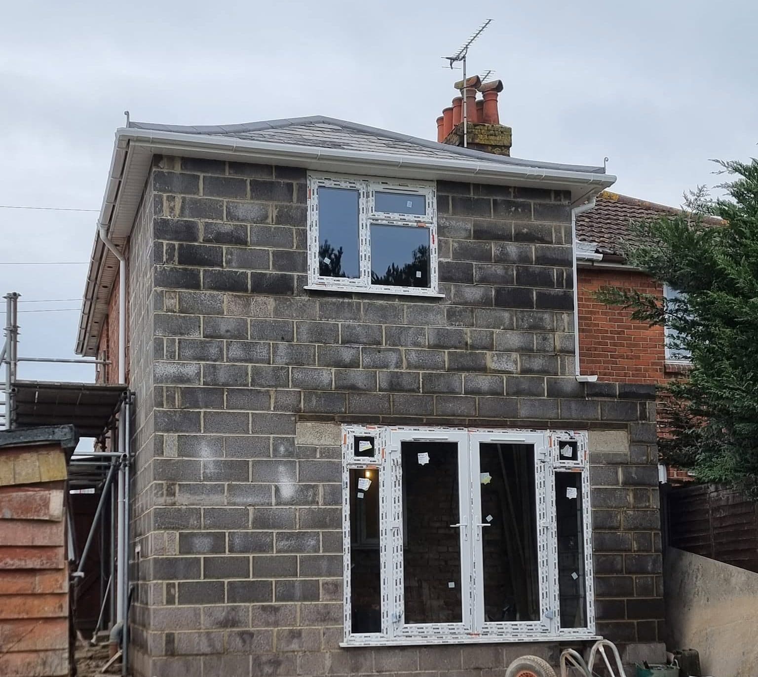 Two-storey rear extension in blockwork with the roof on and new windows and French doors fitted