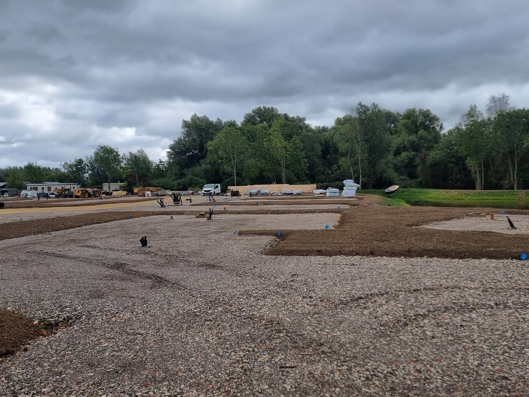 Hardcore building plot with service duct ends showing and topsoil edging, timber packs in the distance
