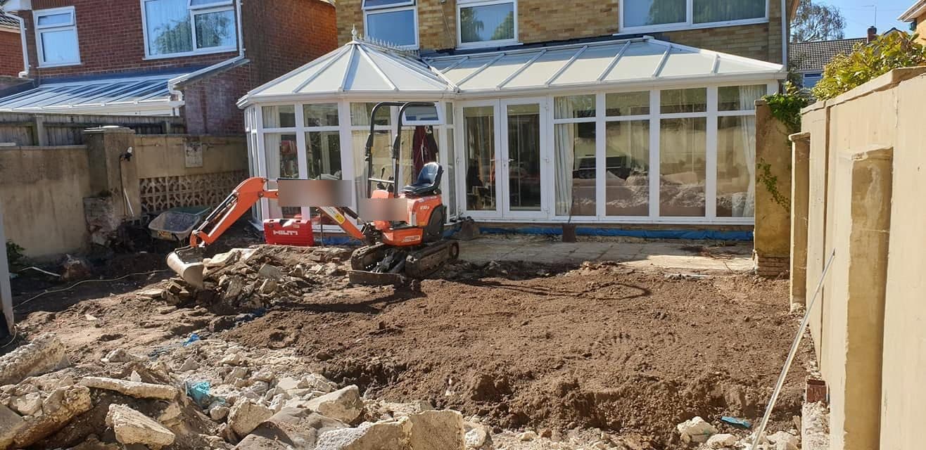 Micro excavator clearing a back garden, broken paving and rubble in front, conservatory behind